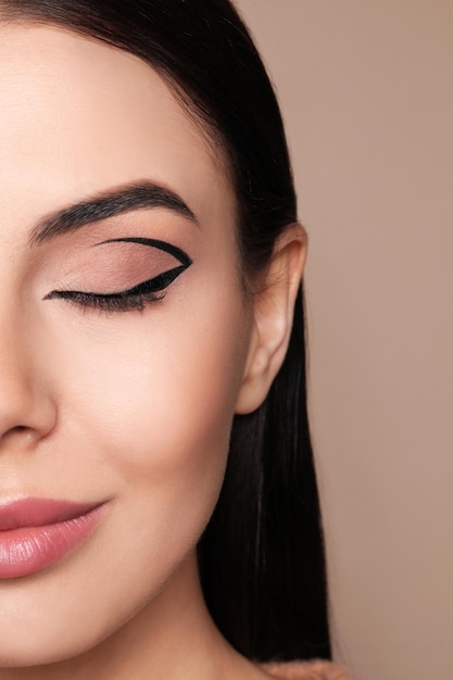 Beautiful woman with black eyeliner on beige background closeup