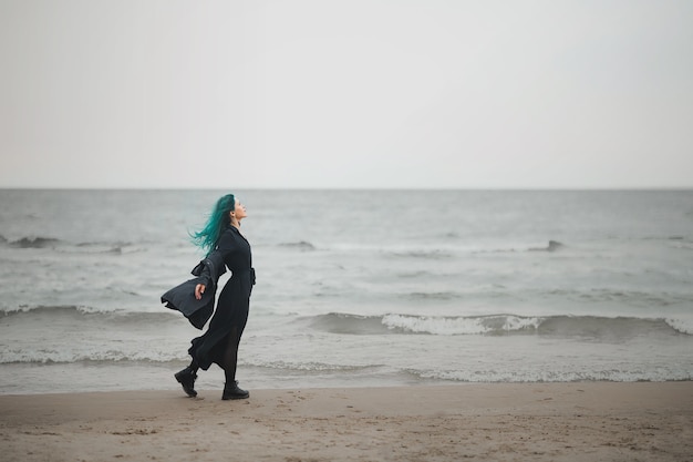 Beautiful woman with blue hair walks along the seashore and enjoys the wind