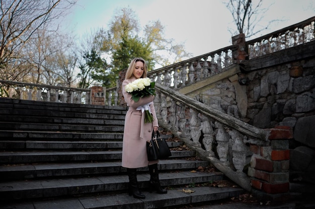 A beautiful woman with a bouquet in her hands stands near an ancient staircase