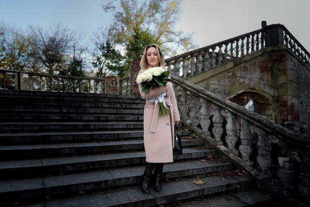 A beautiful woman with a bouquet in her hands stands near an ancient staircase