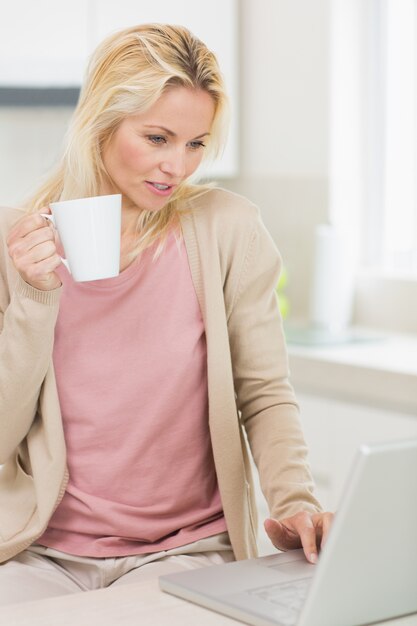 Photo beautiful woman with coffee cup using laptop in kitchen