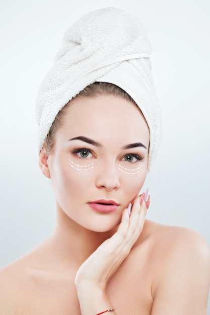 Beautiful woman with dark eyebrows and naked shoulders, wearing white towel on head holding hand with pink manicure