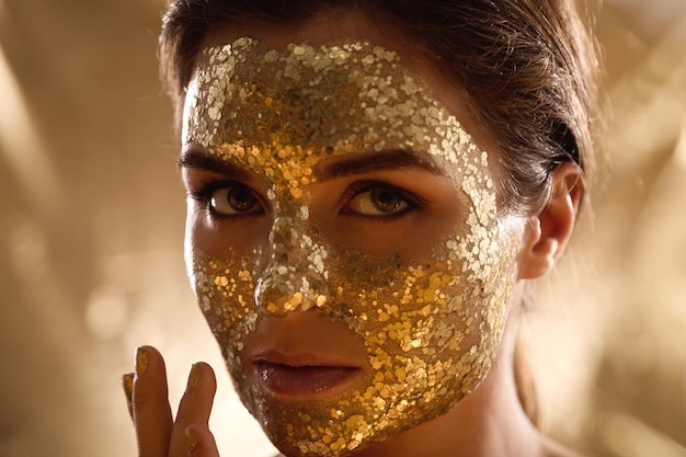 Beautiful woman with golden shining mask on her face for skin treatment