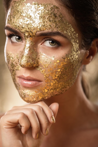 Beautiful woman with golden shining mask on her face for skin treatment