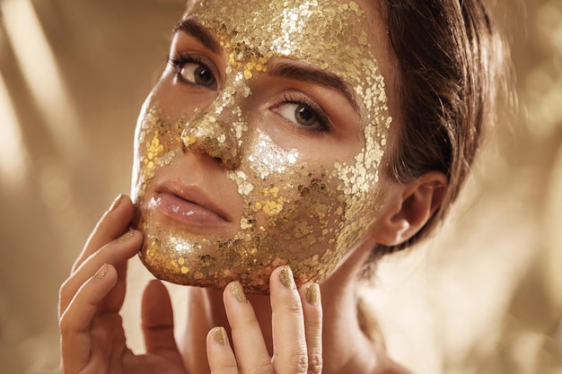 Beautiful woman with golden shining mask on her face for skin treatment