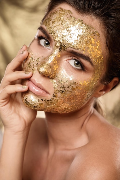 Beautiful woman with golden shining mask on her face for skin treatment