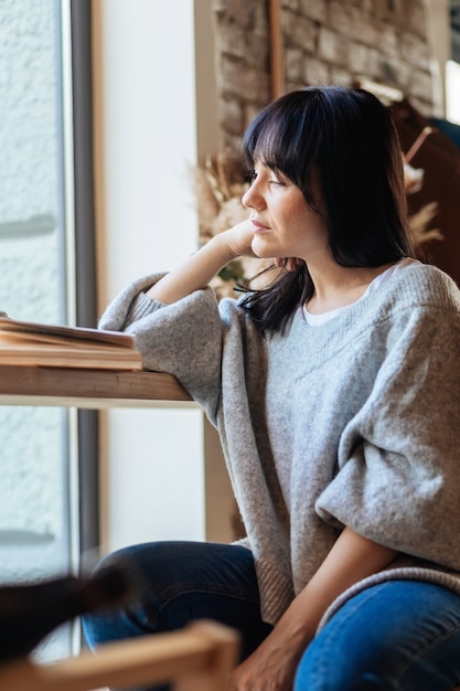 Beautiful woman with hand on chin looking away in cafeteria. Picture of young pretty woman sitting at the table in cafe and reading book.