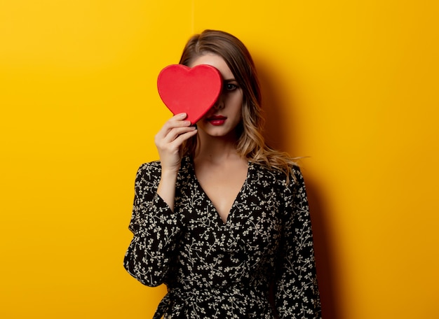 Beautiful woman with heart shape box on yellow wall 