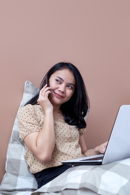 Beautiful woman with laptop on bed on the phone