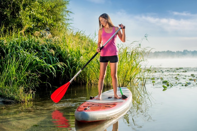 A beautiful woman with an oar swims on a SUP paddle board