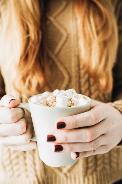 Beautiful woman with red hair hold mug with hot coffee with whipped cream marshmallow and cinnamon