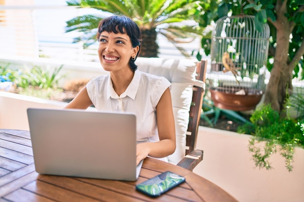 Beautiful woman with short hair sitting at the terrace on a sunny day working from home using laptop