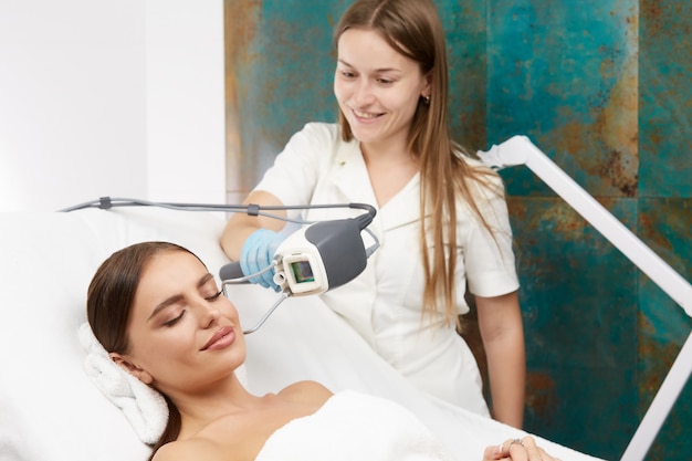 Beautiful woman with smile on face receiving facial treatment with laser in beauty clinic