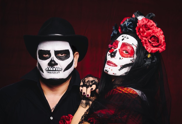 Beautiful woman with a sugar skull makeup with a wreath of flowers on her head and a skeleton man in a black hat