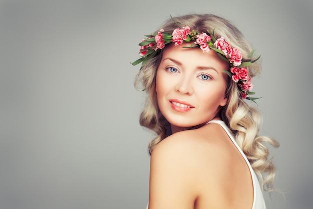 Beautiful Woman with Summer Pink Flowers. Blonde Beauty. Long Permed Curly Hair and Fashion Makeup. Beauty Girl with Flowers Hairstyle.