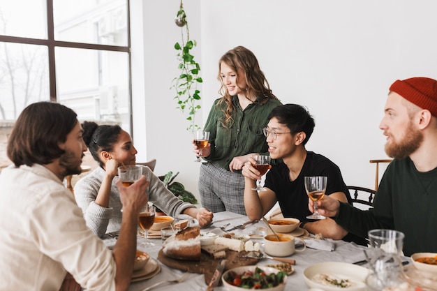 Beautiful woman with wavy hair holding glass of wine in hand happily spending time with colleagues