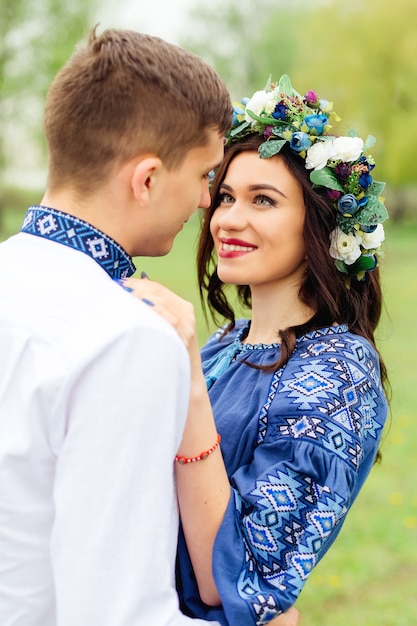 A beautiful woman with a wreath of flowers on her head looks at her boyfriend embracing her