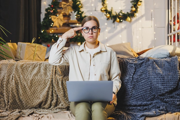 A beautiful woman works at home on New Year's holidays wear comfortable home clothes look at a laptop work remotely for the New Year plaid New Year's winter mood