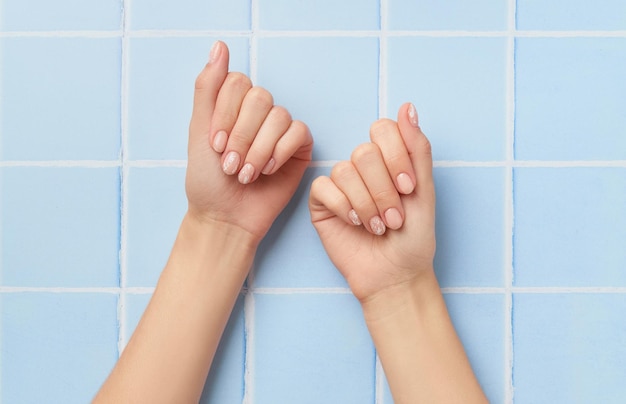 Beautiful womans hands with nude nail design on blue background Manicure pedicure beauty salon concept Empty place for text