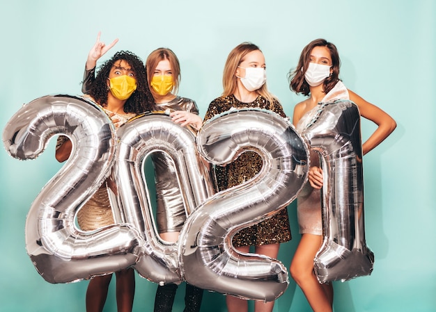 Beautiful Women Celebrating New Year.Happy Gorgeous Female In Stylish Sexy Party Dresses Holding Silver 2021 Balloons, Having Fun At New Year's Eve Party. Holiday Celebration