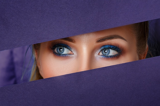 Beautiful women's eyes look in the paper hole, bright make-up .