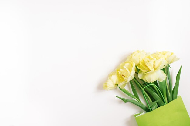 Beautiful yellow tulip flowers in a green paper bag with space for text The concept of sales spring discounts shopping and environmentally friendly packaging