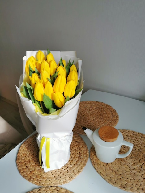 Beautiful yellow tulips on a white table with a teapot