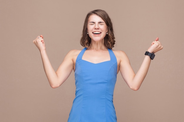 Beautiful young adult business woman rejoicing her win. Studio shot, light brown background