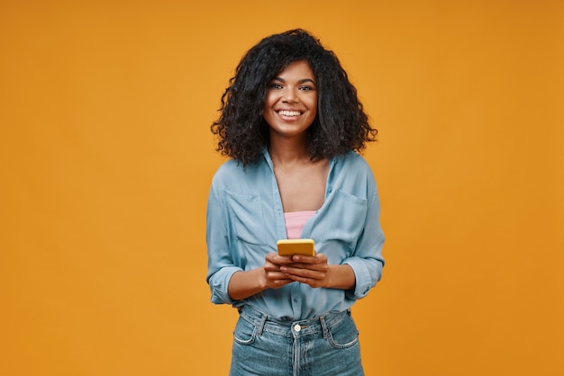 Beautiful young African woman in casual clothing using smart phone and smiling