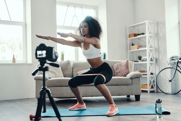 Beautiful young African woman crouching using strap while making social media video