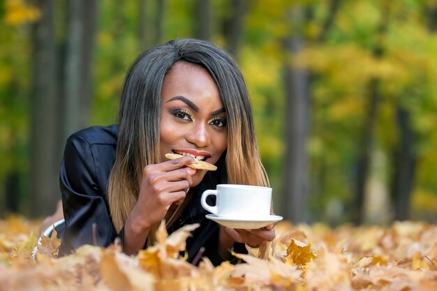 Beautiful young African woman eating cookies and drinking coffee in the forest