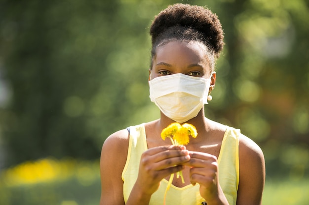 Beautiful young African woman in medical mask with flowers in her hands