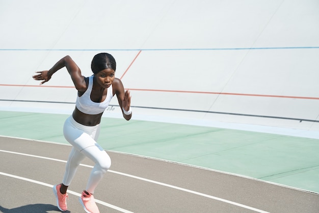 Beautiful young african woman in sports clothing running on track outdoors