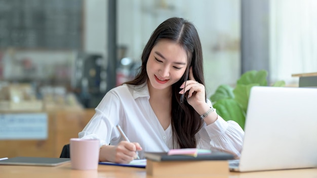 Beautiful young Asian businesswoman charming smiling and talking on the mobile phone in the office.