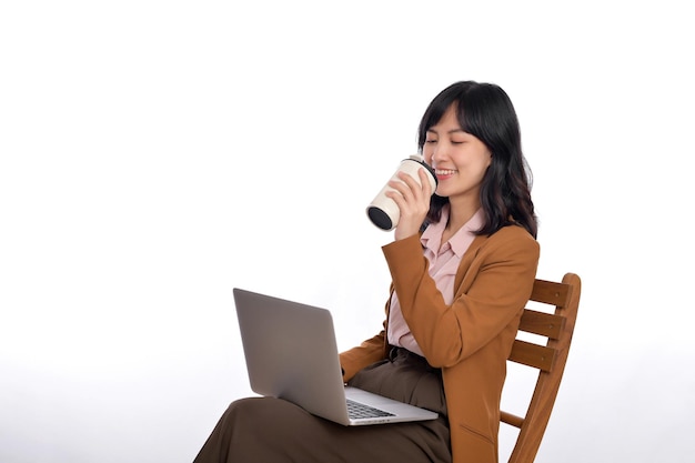 Beautiful young asian businesswoman using computer laptop sitting on white chair and drinking coffee isolate on white background