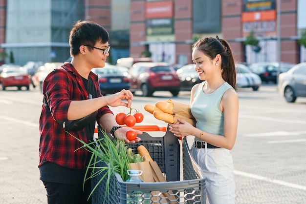 Beautiful young asian couple checking purchased food in the shopping cart near the big store