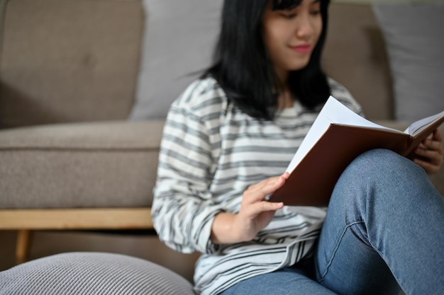 Beautiful young Asian female reading a book while relaxing in her living room