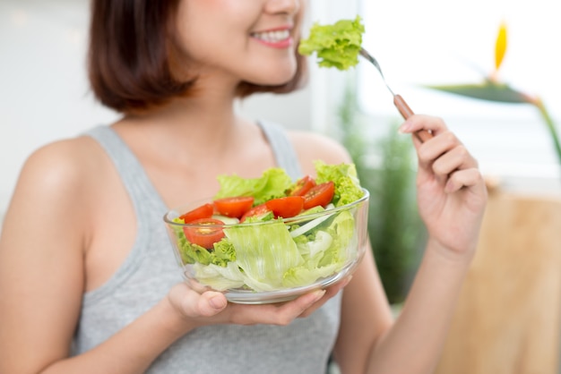 Beautiful young asian girl eating salad. smiling happy girl eating healthy food.