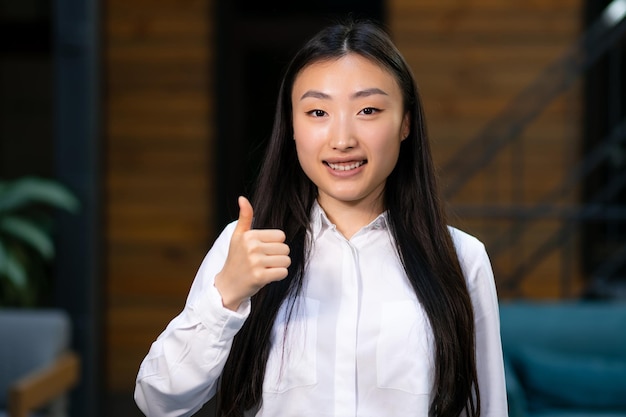 Beautiful young asian girl smiling and showing thumb up in office