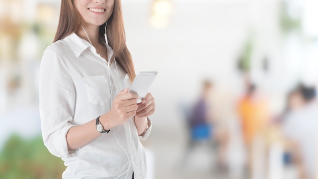 Beautiful young Asian girl using smart phone with earpiece in restaurant background