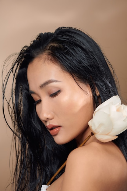 Beautiful young asian girl with natural make-up and wet hair posing in the studio on a beige background