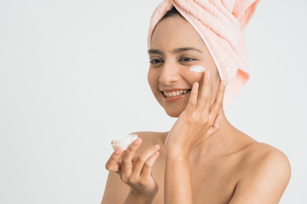 Beautiful young asian woman applying cosmetic cream on her face