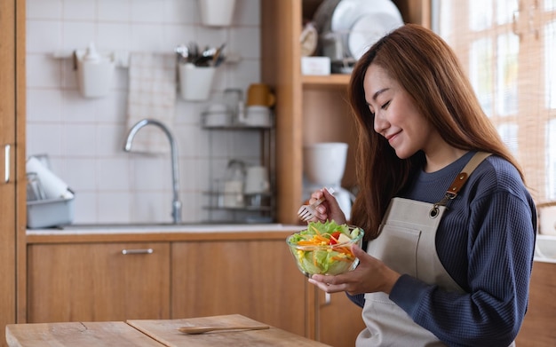 A beautiful young asian woman cooking and eating fresh mixed vegetables salad in the kitchen at home