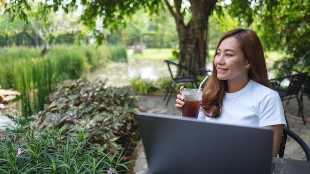 A beautiful young asian woman drinking coffee while take a break from working on laptop computer in the park