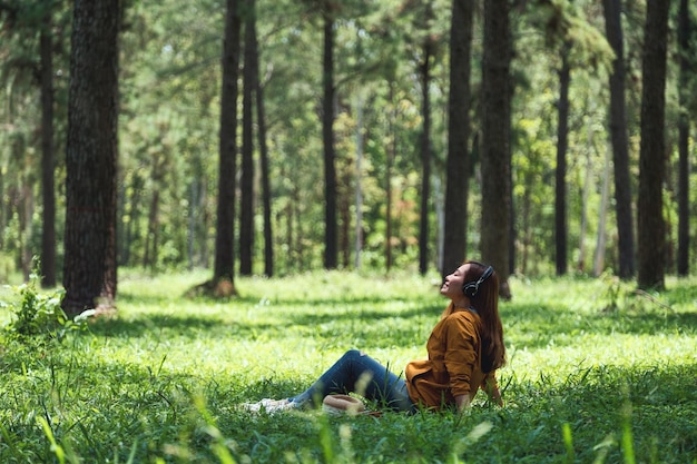 A beautiful young asian woman enjoy listening to music with headphone with feeling happy and relaxed in the park