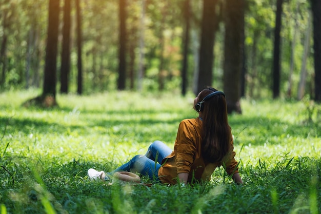 A beautiful young asian woman enjoy listening to music with headphone with feeling happy and relaxed in the park