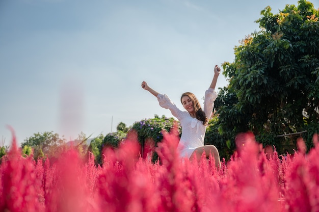 Beautiful young asian woman enjoying with raising arms in cockscomb red flower garden