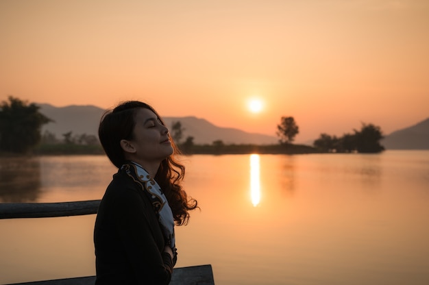 Beautiful young asian woman enjoying with sunrise on mountain lake at the morning