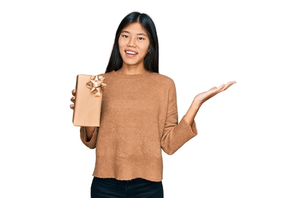 Photo beautiful young asian woman holding gift celebrating victory with happy smile and winner expression with raised hands