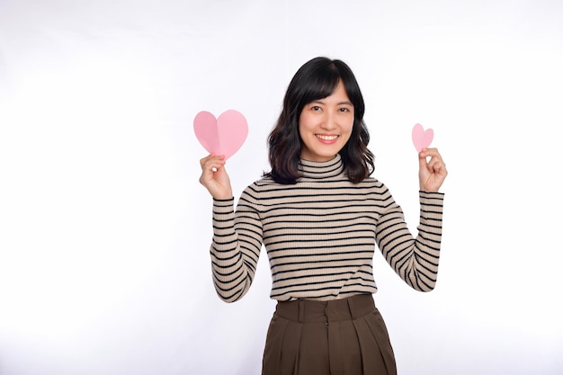 Beautiful young asian woman holding a paper heart while standing against white background Beautiful young asian woman with paper heart